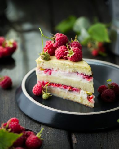 Eine leckere Torte mit Himbeeren und Sahne, auf einem schwarzen Teller angerichtet.